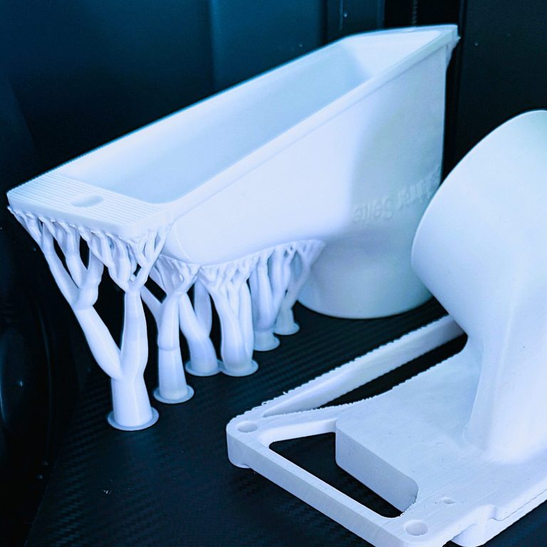 3D Druck FDM Fahrzeug Bauteil Zwei weiße 3D-gedruckte Objekte in einer dunklen Umgebung.